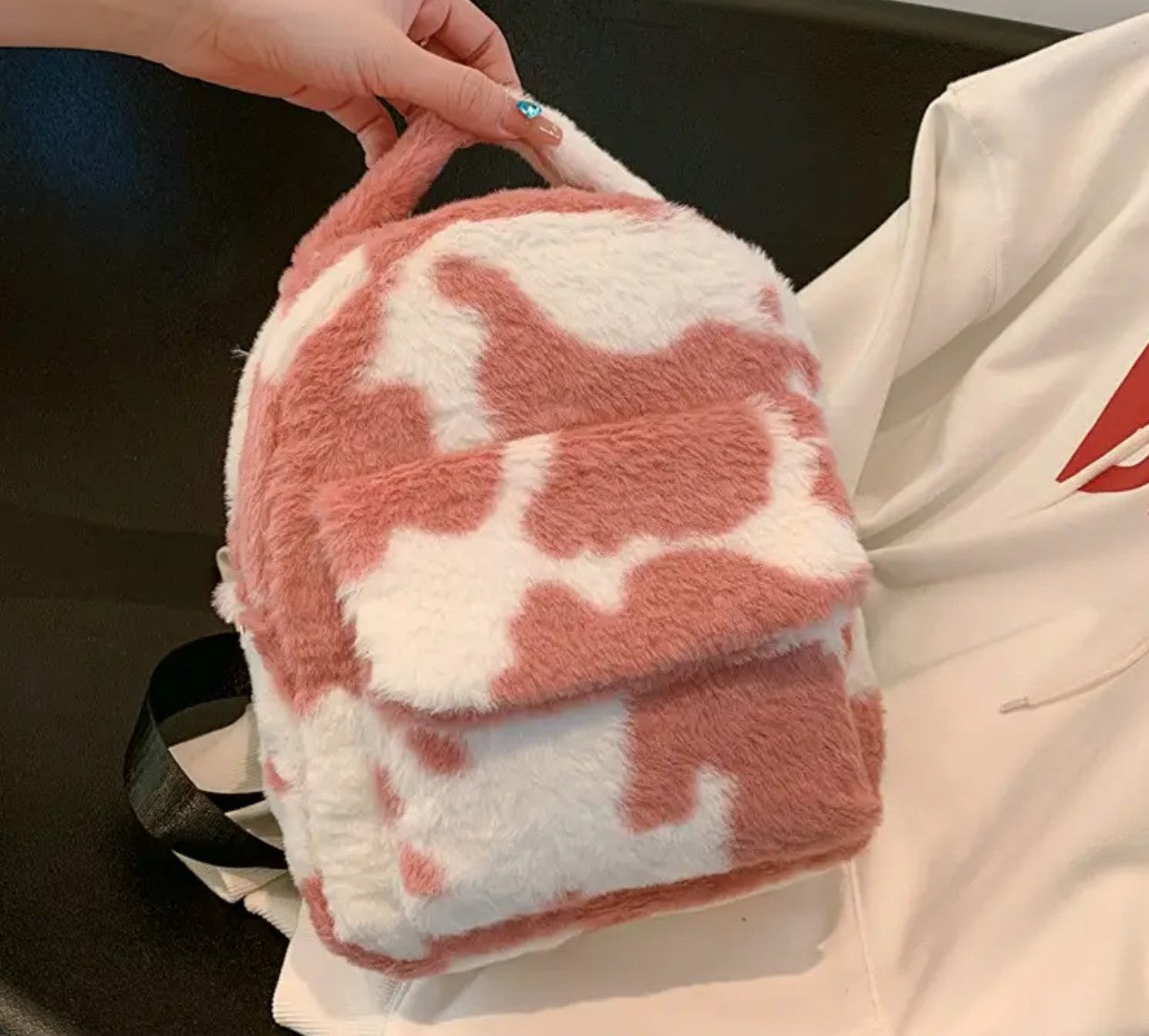 A pink and white cow print plush backpack