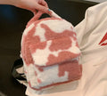 A pink and white cow print plush backpack