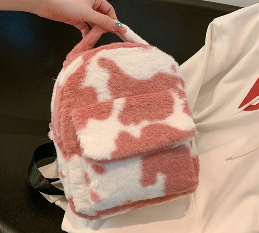 A pink and white cow print plush backpack